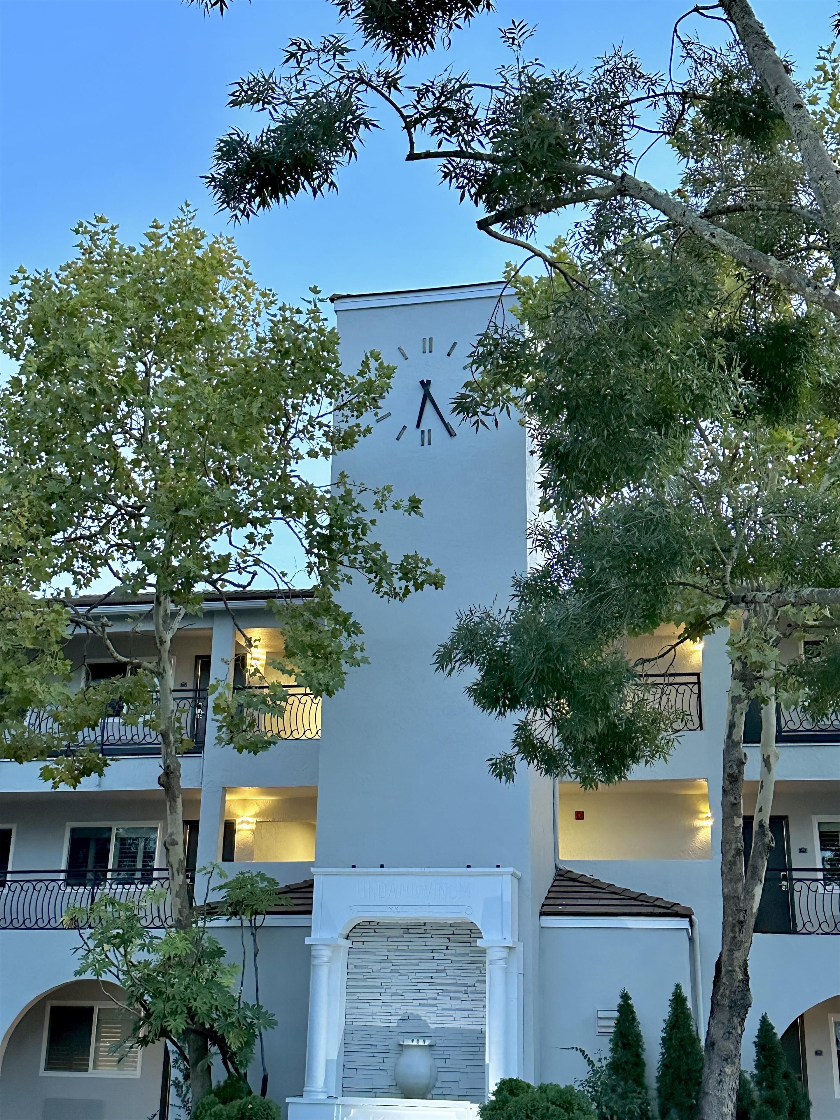 Un bâtiment orné d’une horloge sur sa façade, entouré d’arbres et de balcons.