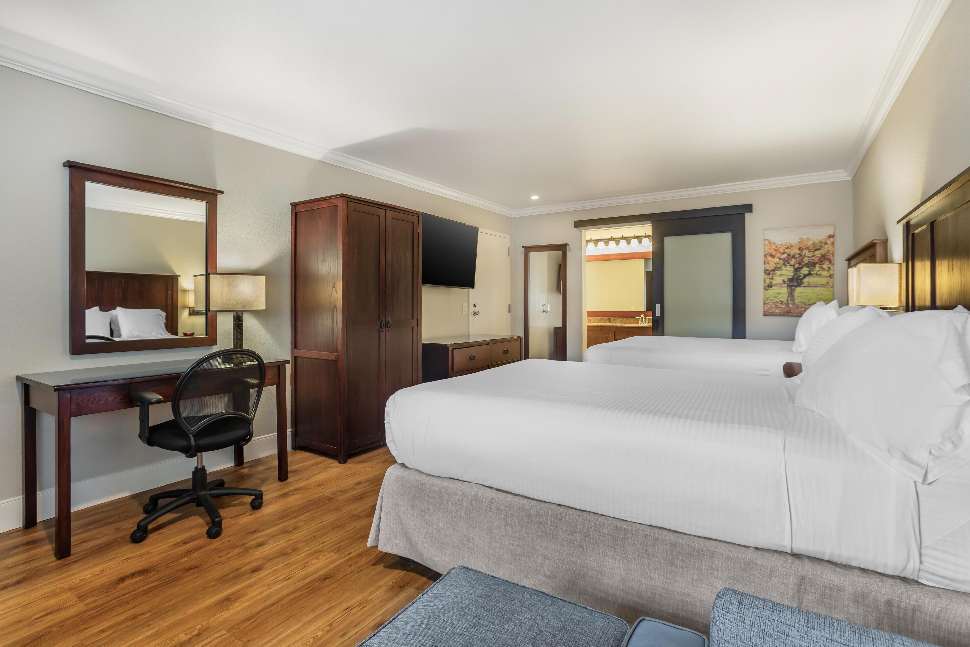 A hotel room with a large bed, a desk with a chair, a wardrobe, and a television.