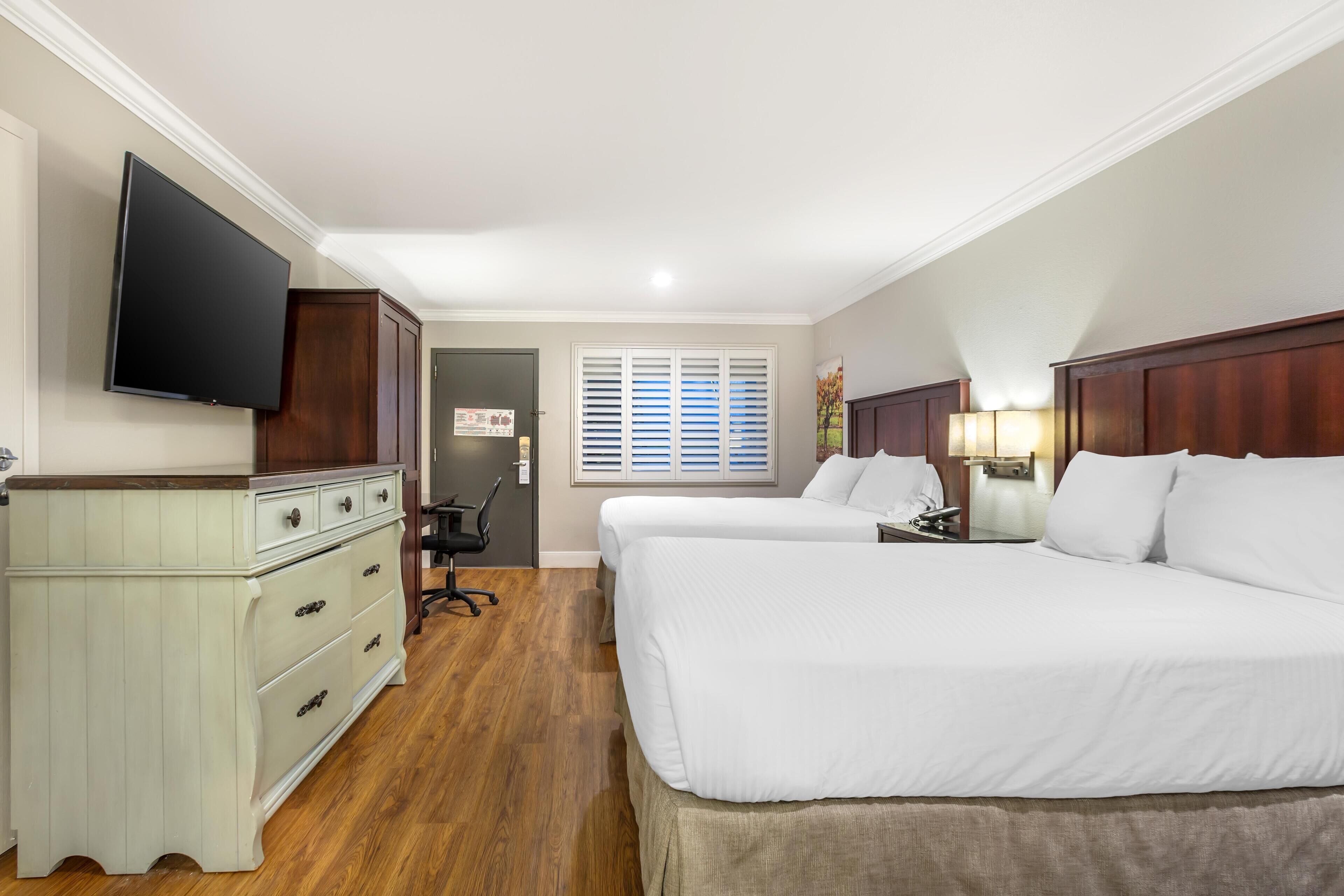 A hotel room with two beds, a TV, a desk, and a chair.
