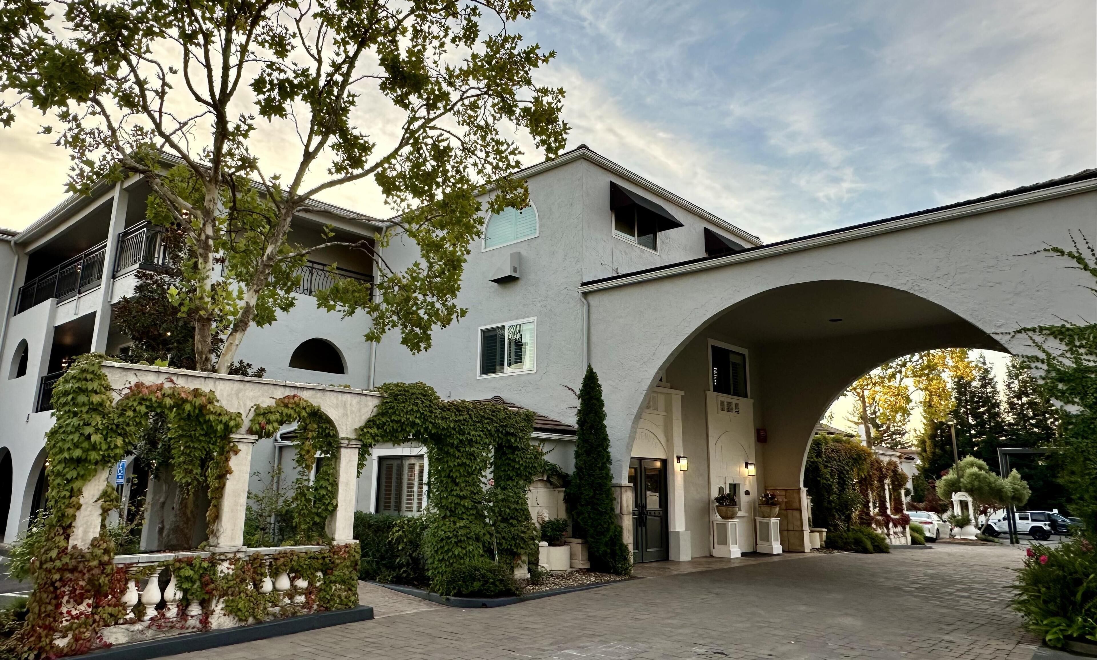 A multi-story building with a covered entrance, surrounded by greenery and a paved driveway.