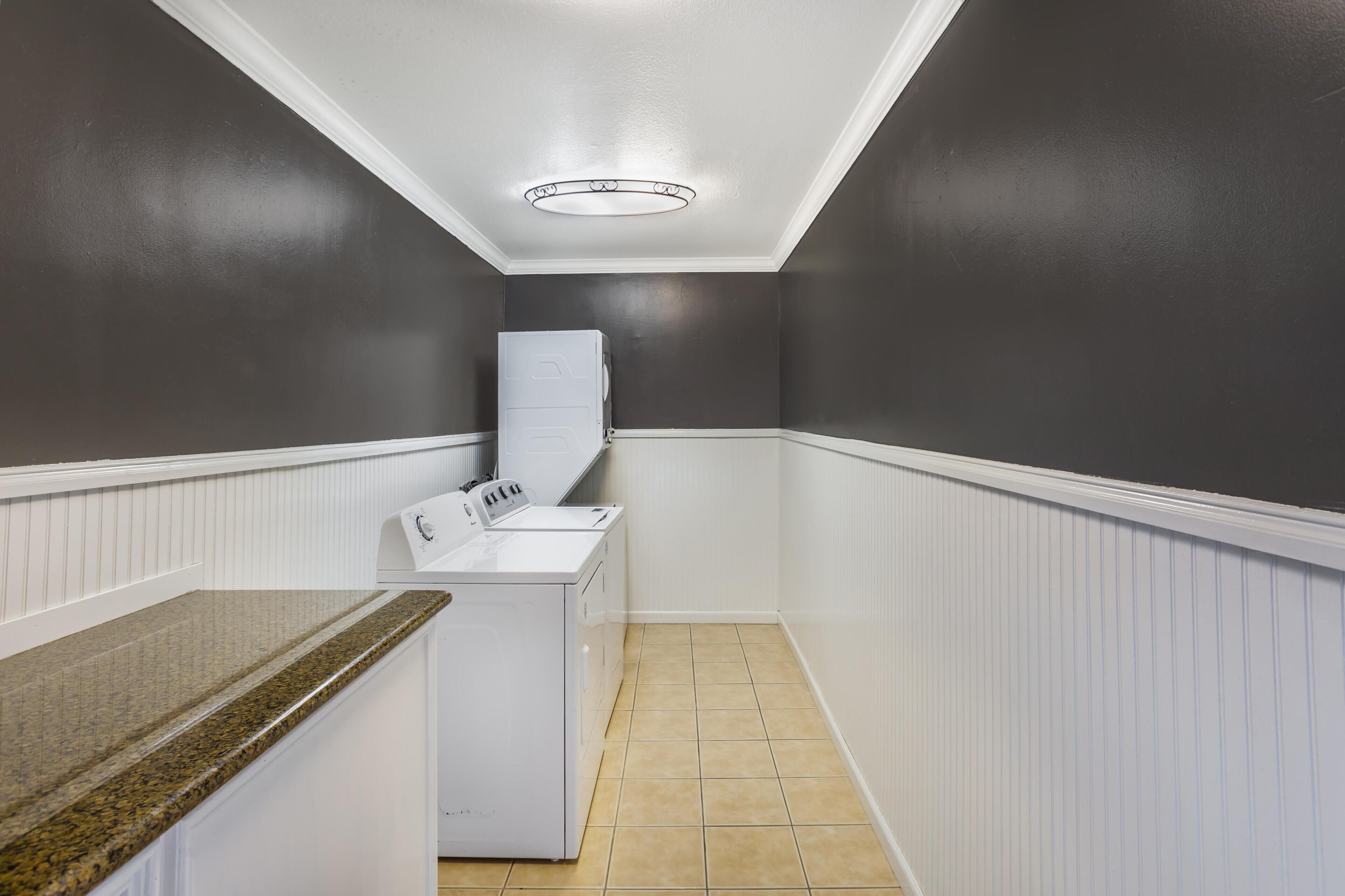 A laundry room with a washing machine and dryer, white wainscoting, and a tiled floor.
