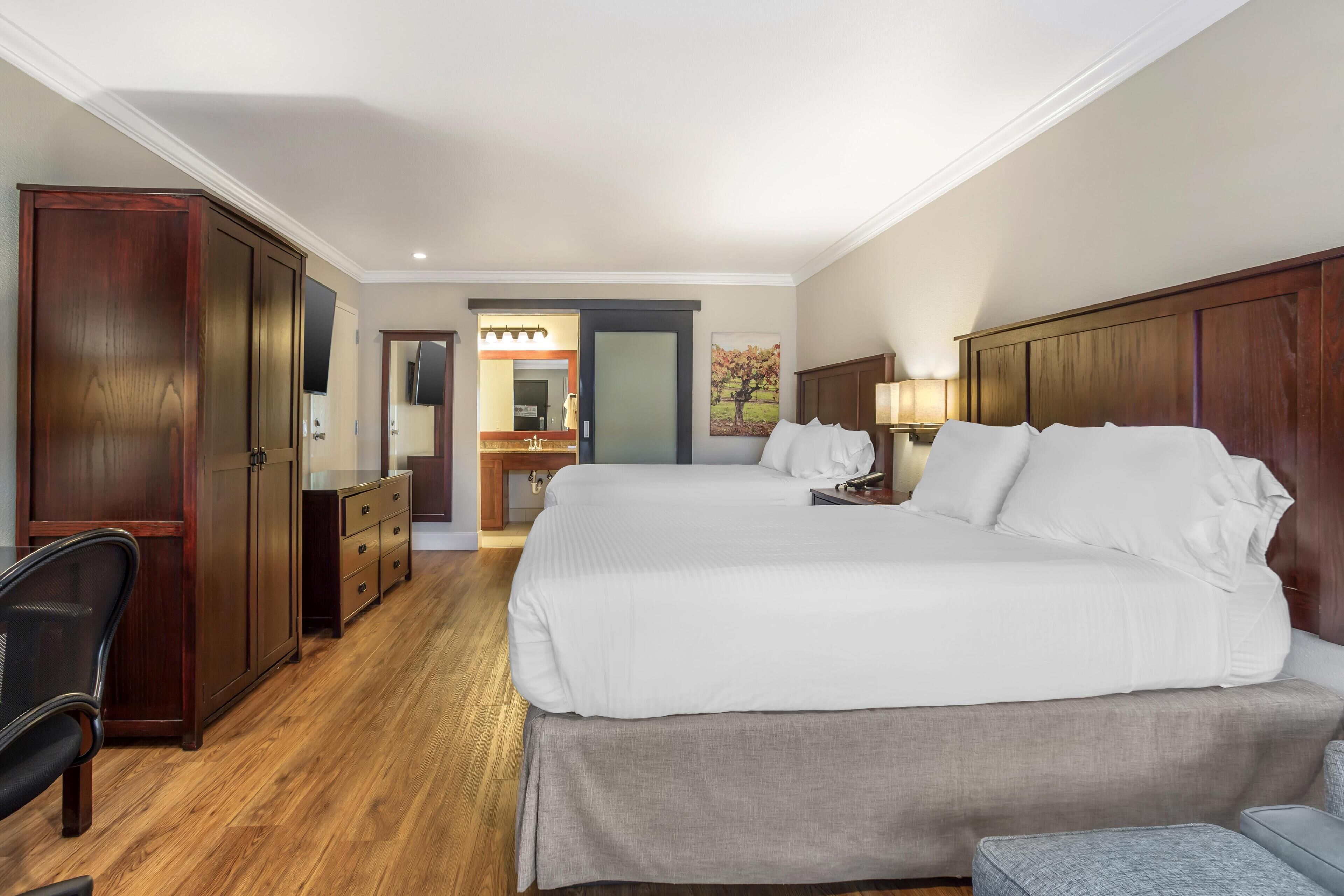 Ein Hotelzimmer mit einem großen Bett, einem Schreibtisch, einem Sessel, einem Kleiderschrank und einem durchgegangenen Badezimmer.