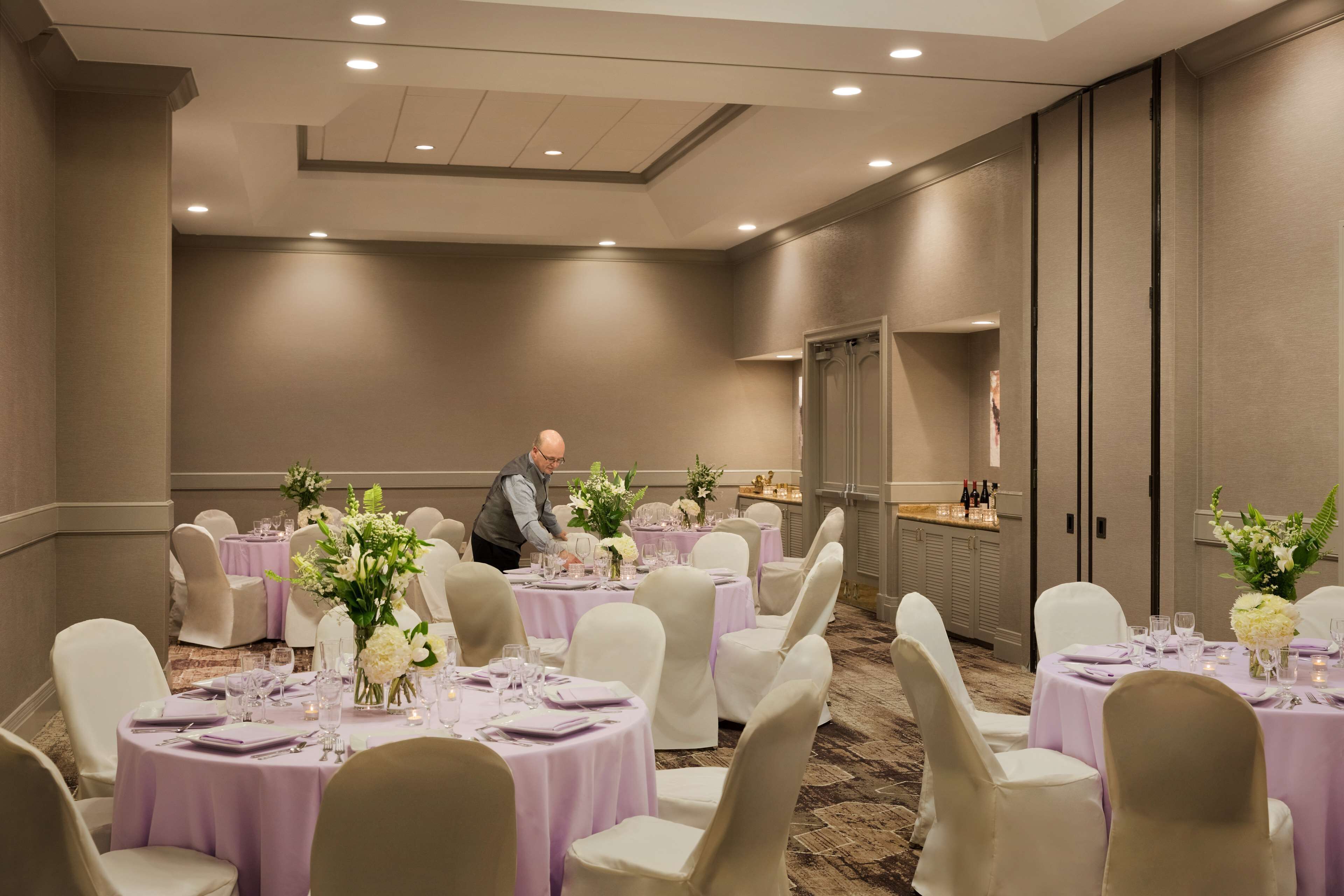 A banquet hall with round tables covered in purple tablecloths, white chairs, and floral centerpieces.
