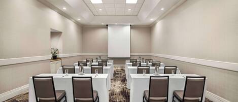 A conference room with multiple tables, chairs, and a projector screen.