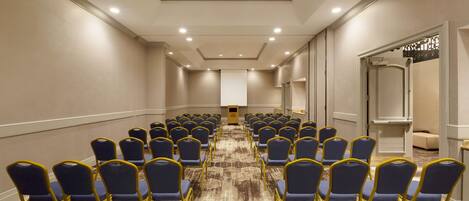 Un salón de conferencias con filas de sillas azules y suelo alfombrado.