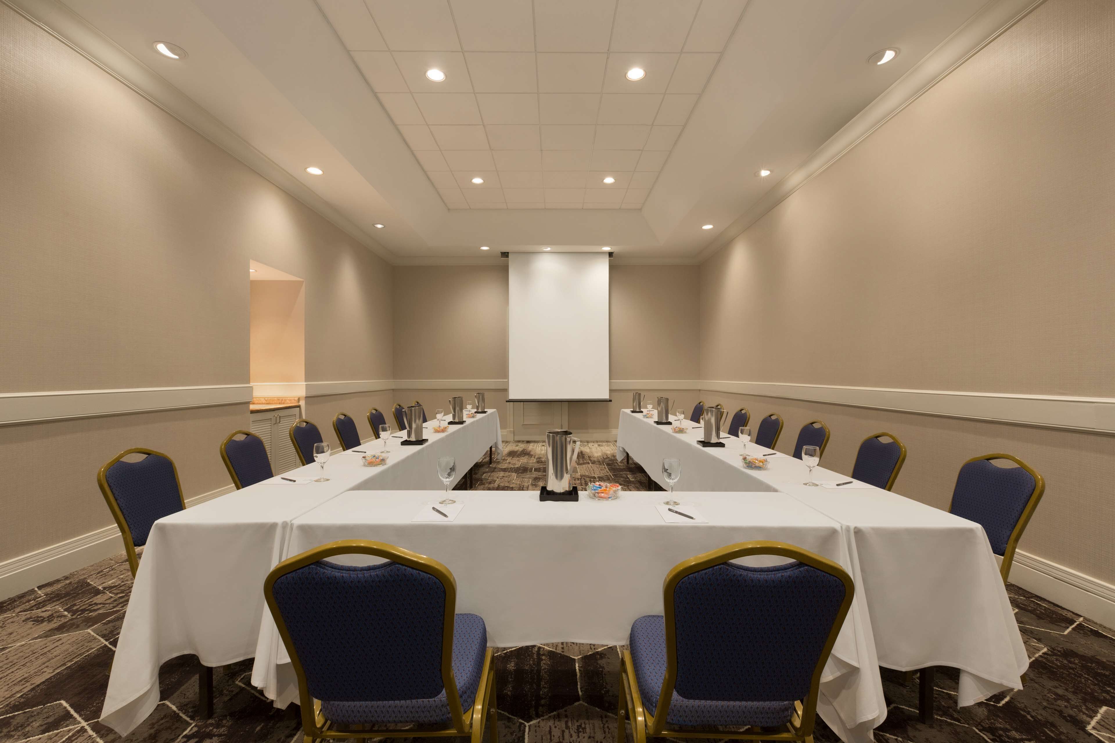 Una sala de conferències amb una taula llarga, cadires blaves i una pantalla de projector al capdavant.