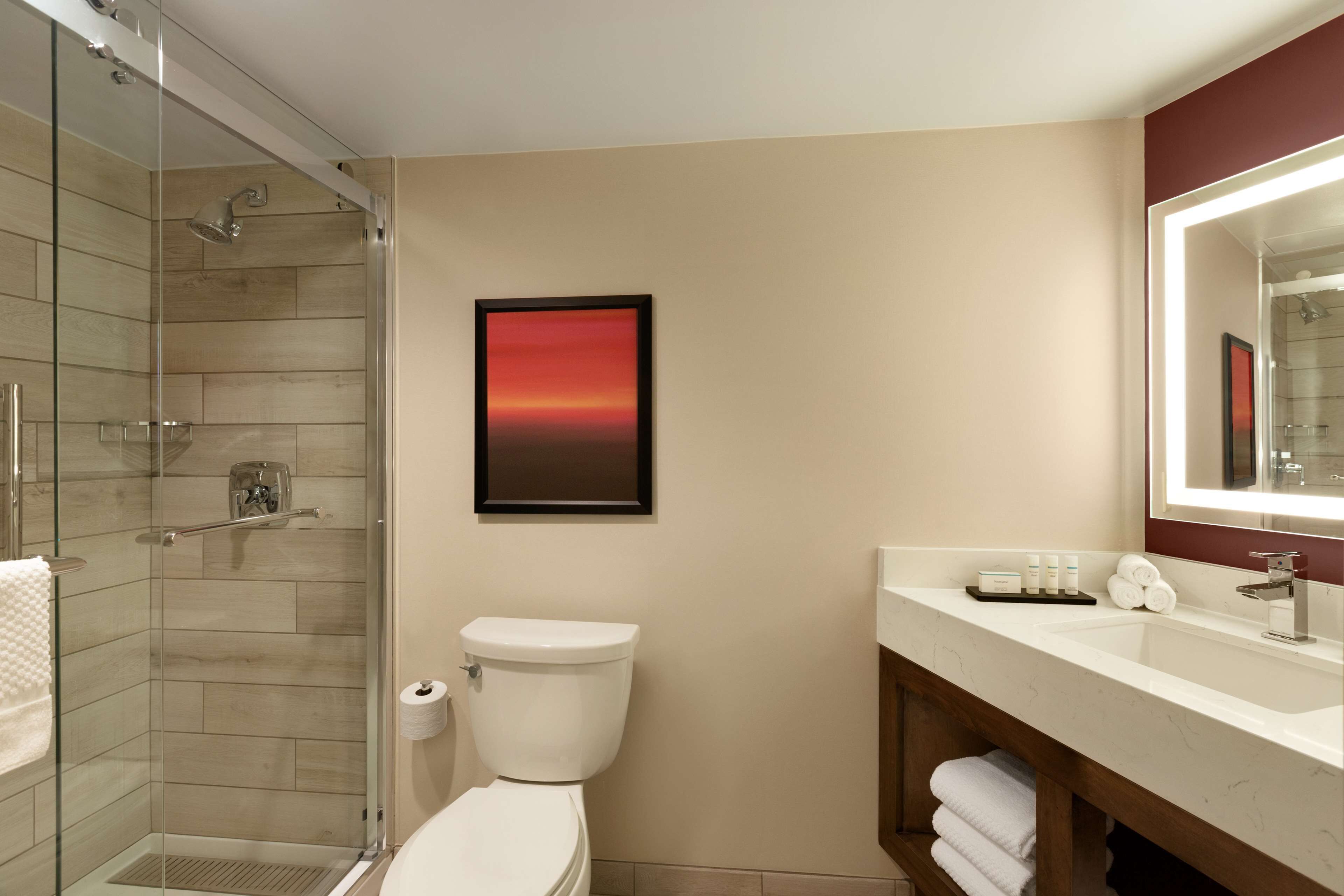 A modern bathroom with a glass-enclosed shower, a white toilet, a marble sink, and a framed picture on the wall.
