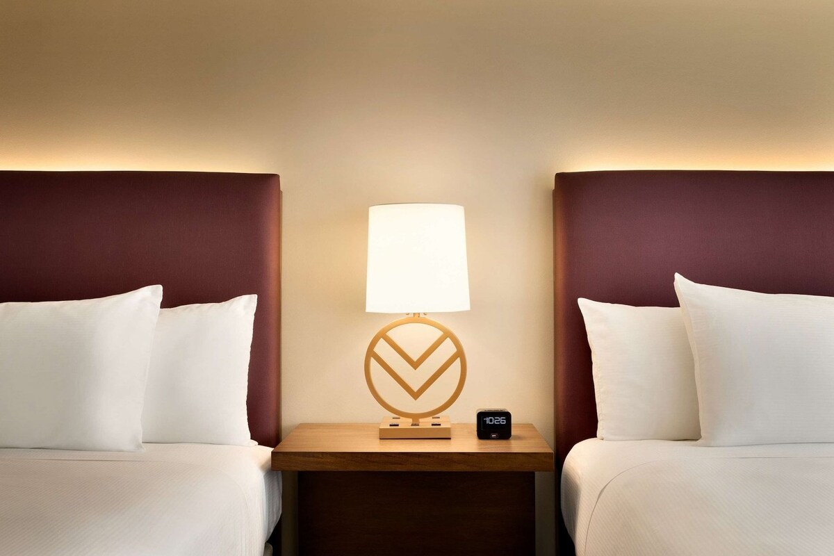 A hotel room with two beds, a nightstand with a lamp, and a clock.