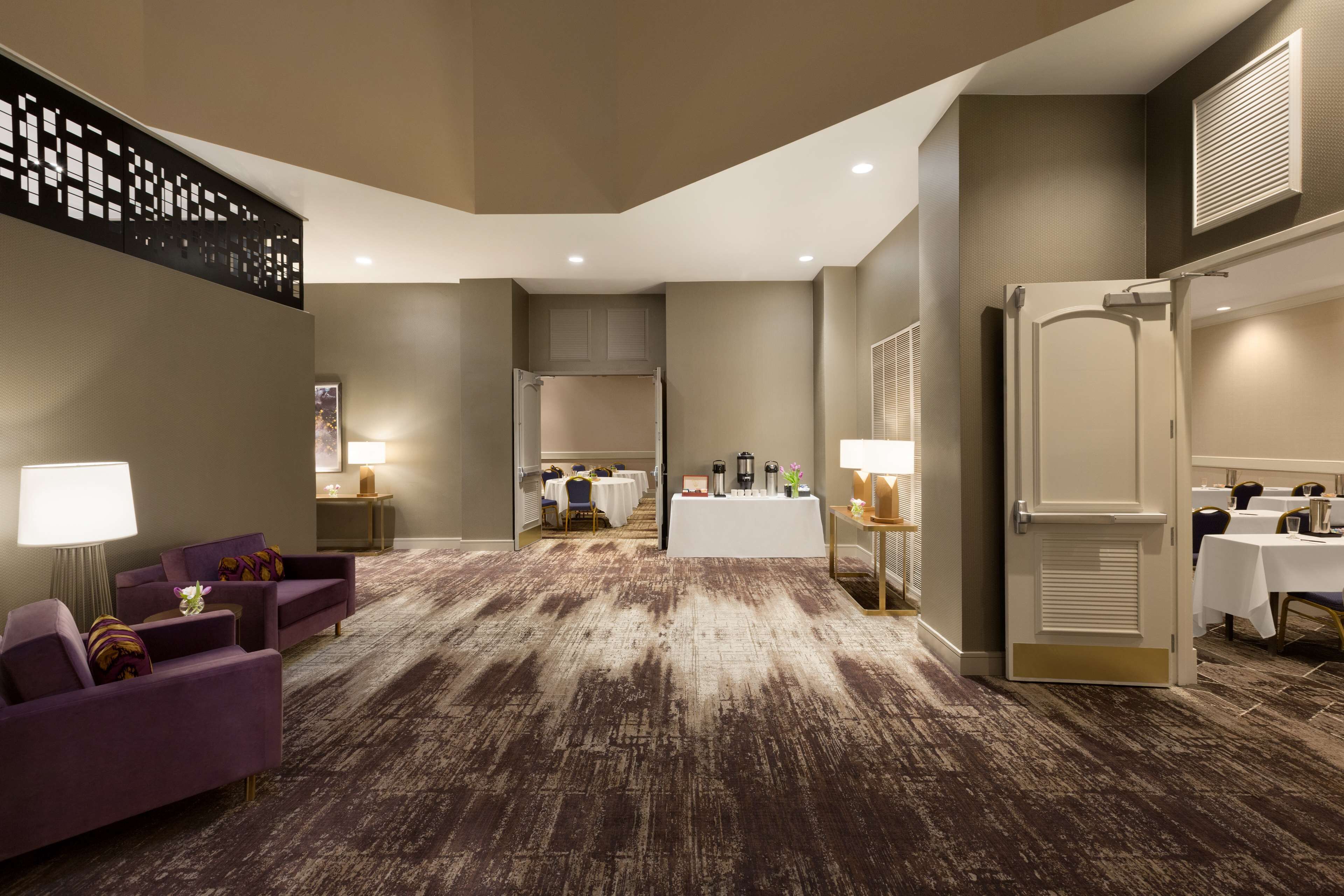 A hotel lobby with purple armchairs, a reception desk, and a dining area with tables and chairs.