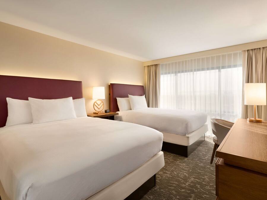 A hotel room with two beds, a desk, and a TV.
