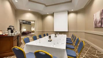 A conference room with a long table, blue chairs, a projector screen, and a coffee station.