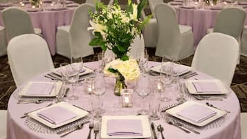 Una mesa redonda dispuesta con platos blancos, cubiertos y vasos transparentes, rodeada de sillas blancas.