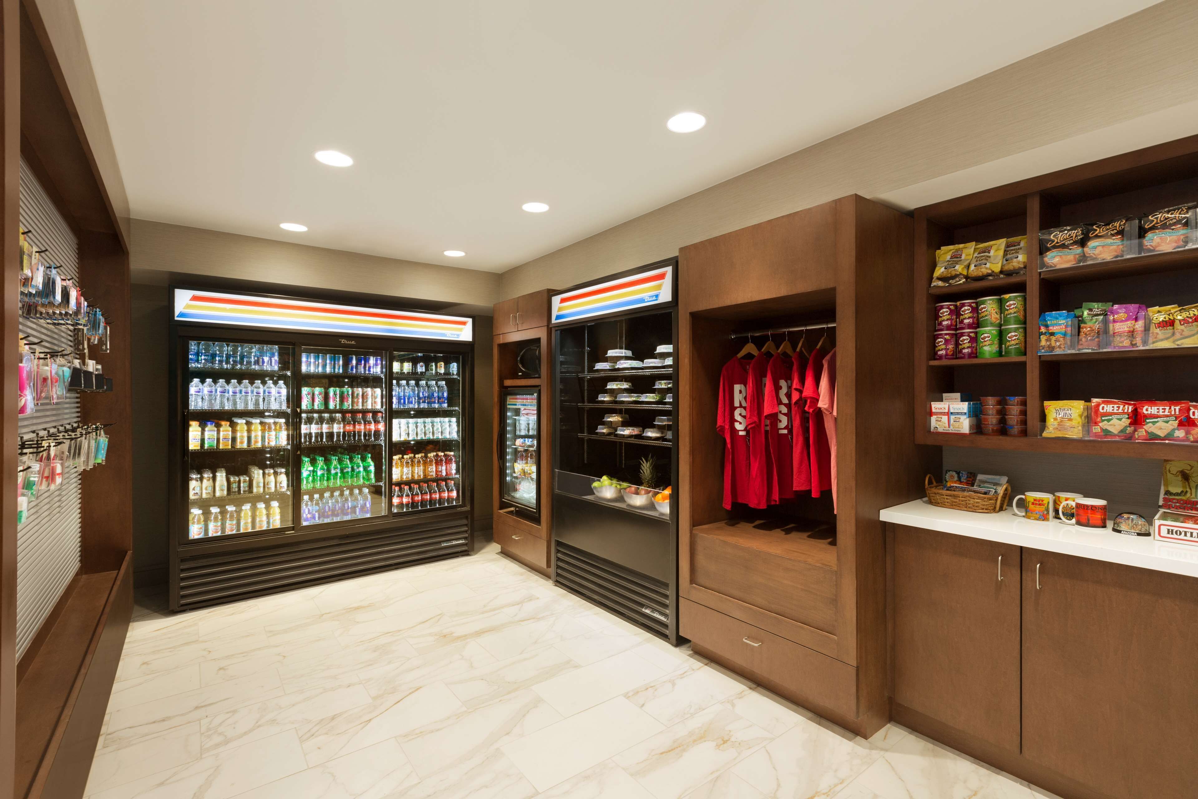 A well-lit, spacious room with a marble floor, a refrigerator stocked with beverages, a shelf with snacks, and a rack of red shirts.