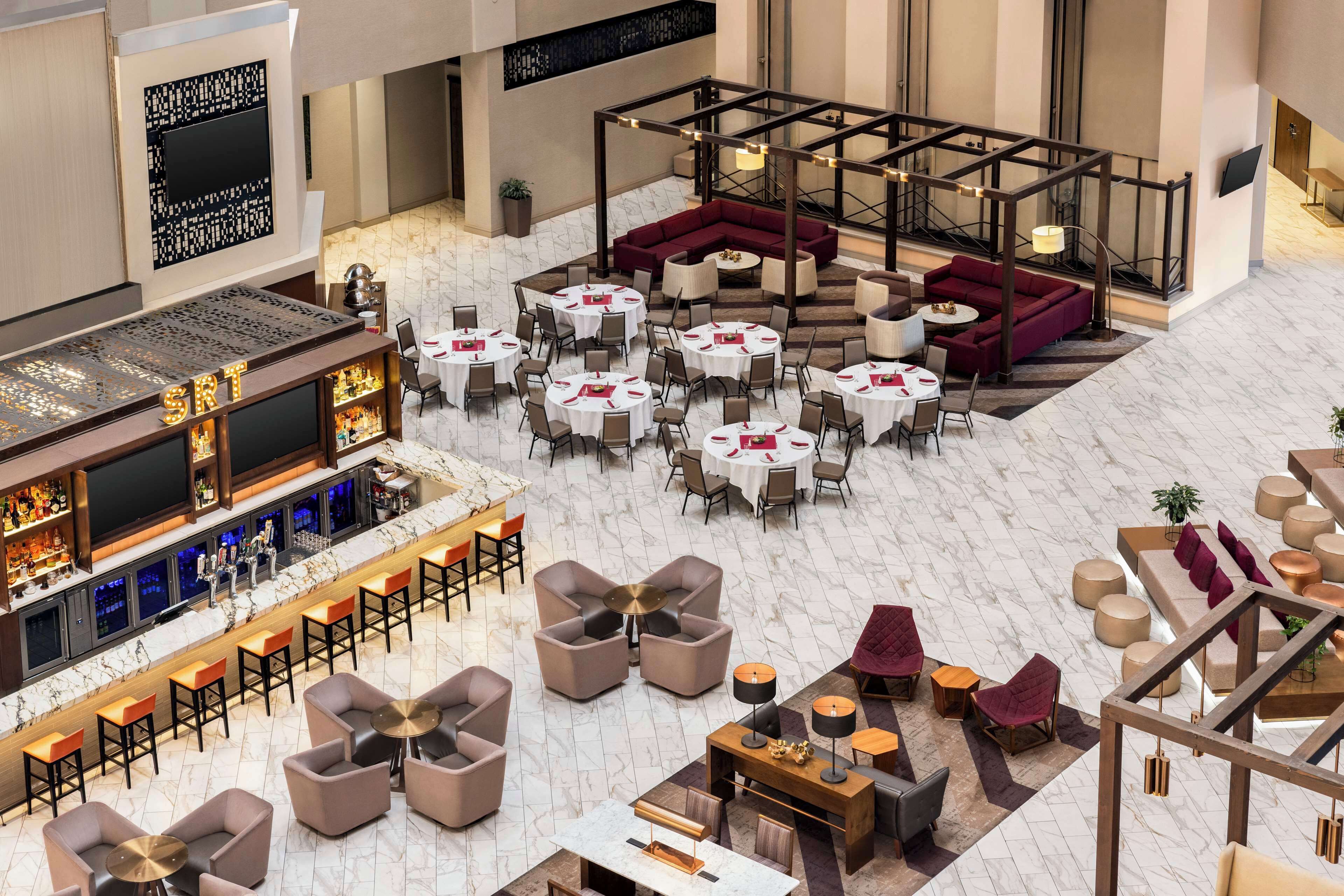 A spacious hotel lobby with multiple seating areas, a bar, and a staircase.