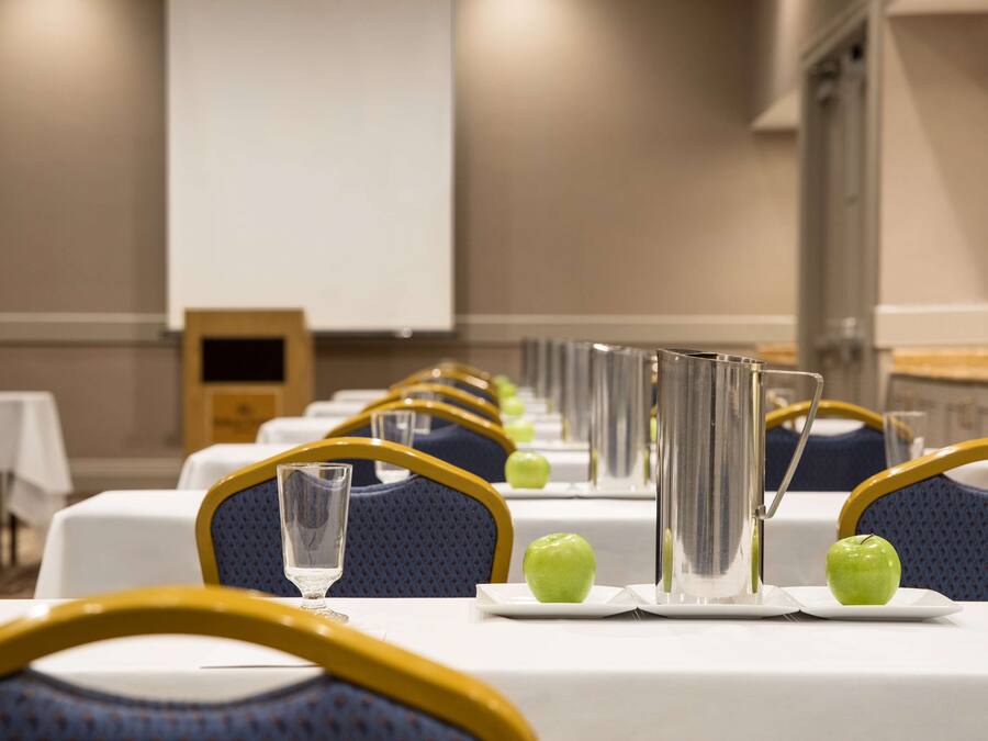 A conference room with tables set for a meeting, each with a glass of water, a plate with an apple, and a silver vase.