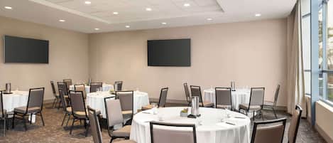 A conference room with round tables, chairs, and a carpeted floor.