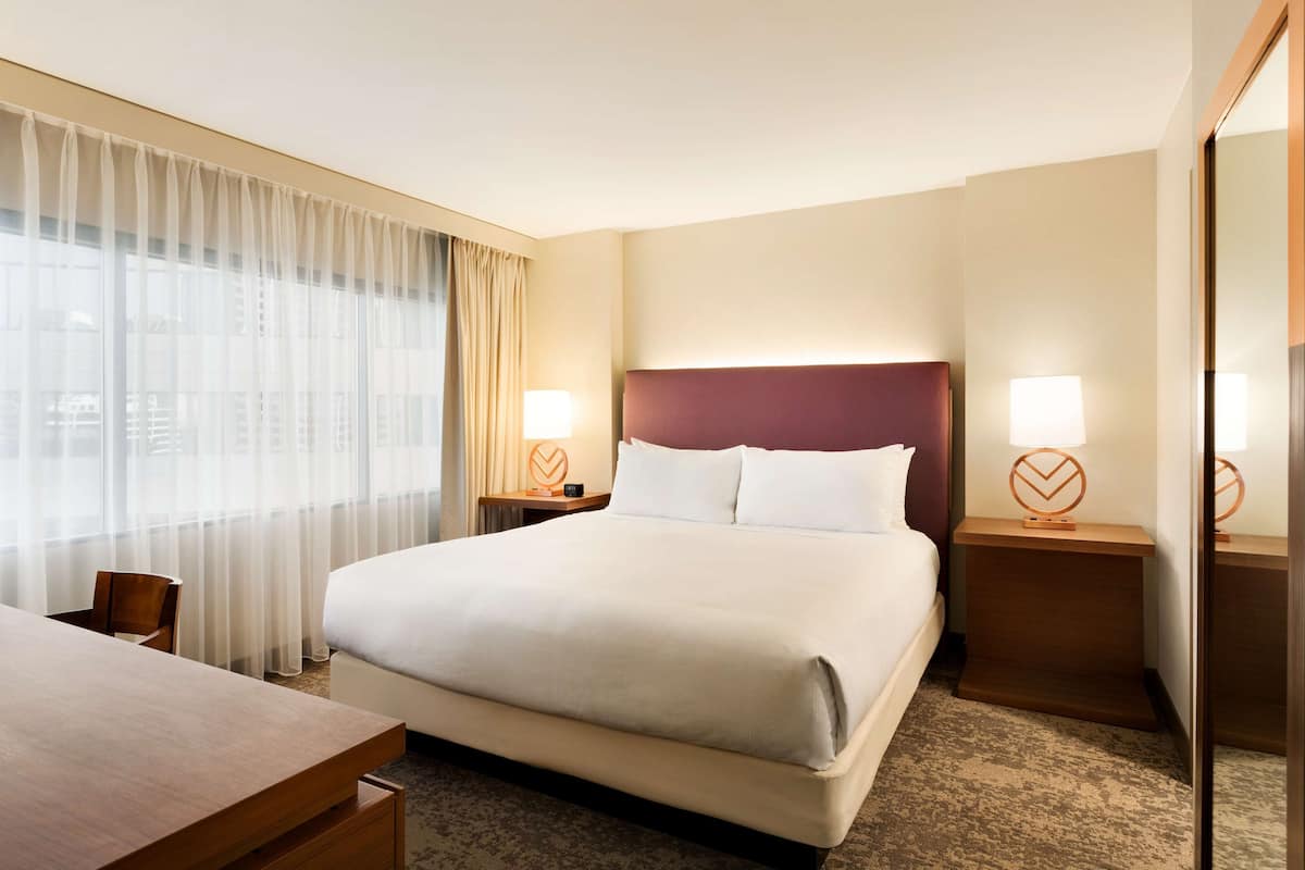 Ein Hotelzimmer mit einem großen Bett, zwei Nachttischen mit Lampen, einem Holztisch und einem Stuhl.