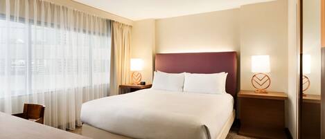 Una habitación de hotel con una cama grande, dos mesitas de noche con lámparas, un escritorio de madera y una silla.