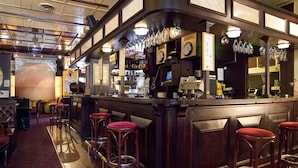 Una zona de bar con mostrador de madera, taburetes y diversos utensilios.