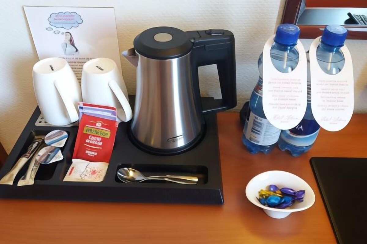 Hotelkamer met een dienblad met waterkoker, kopjes, een zakje snacks, een lepel en een schaaltje snoep.