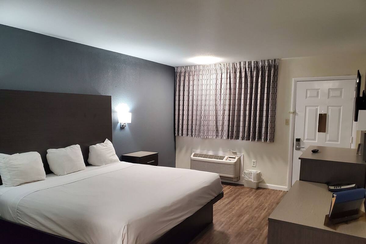 Una habitación de hotel con cama, mesita de noche, aire acondicionado y un escritorio con silla.