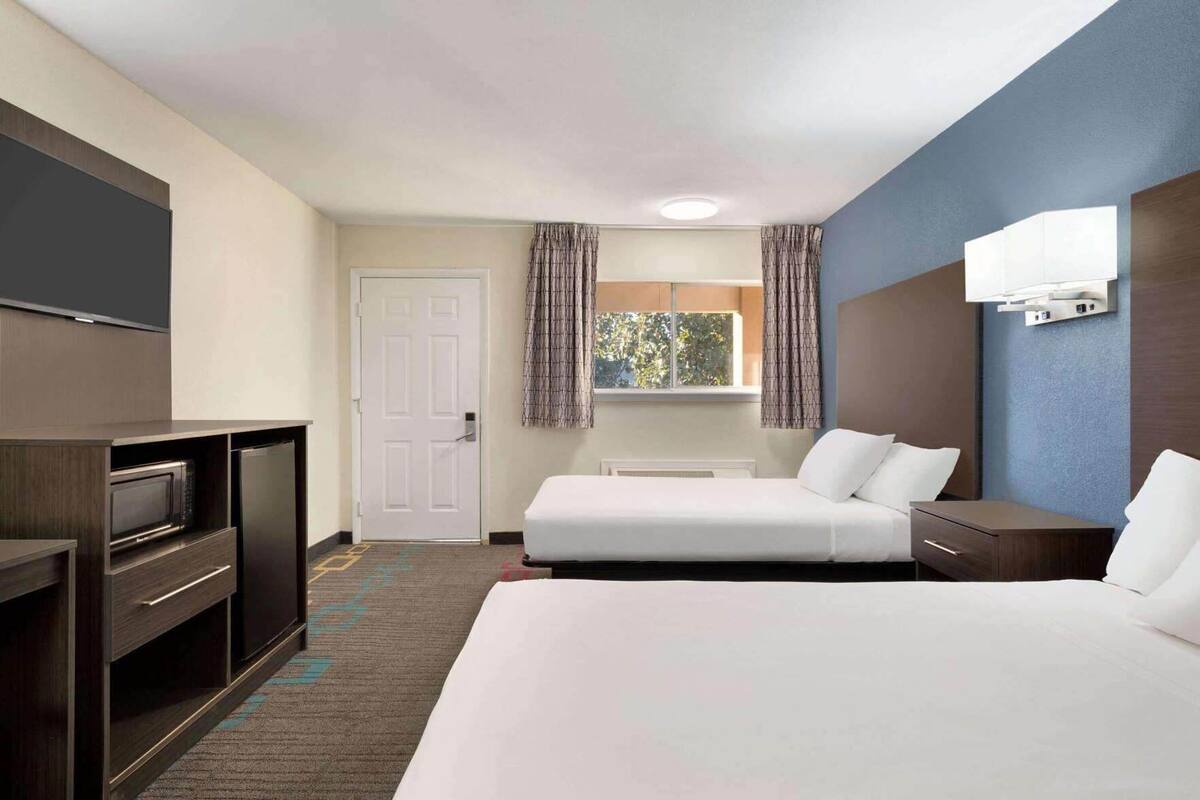 Habitación de hotel con cama, escritorio, televisor de pantalla plana, puerta y ventana con cortinas.