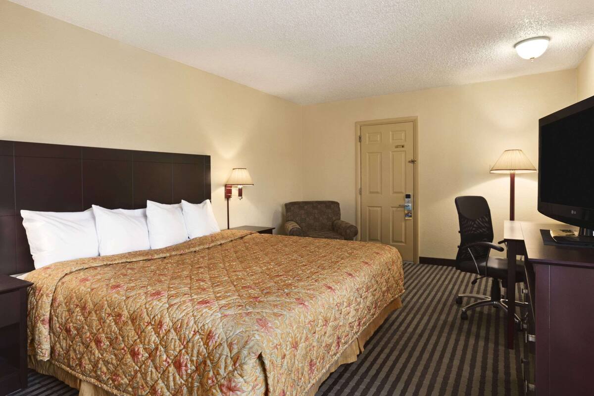 Una habitación de hotel con una cama grande, un escritorio con una computadora, una silla y un televisor.
