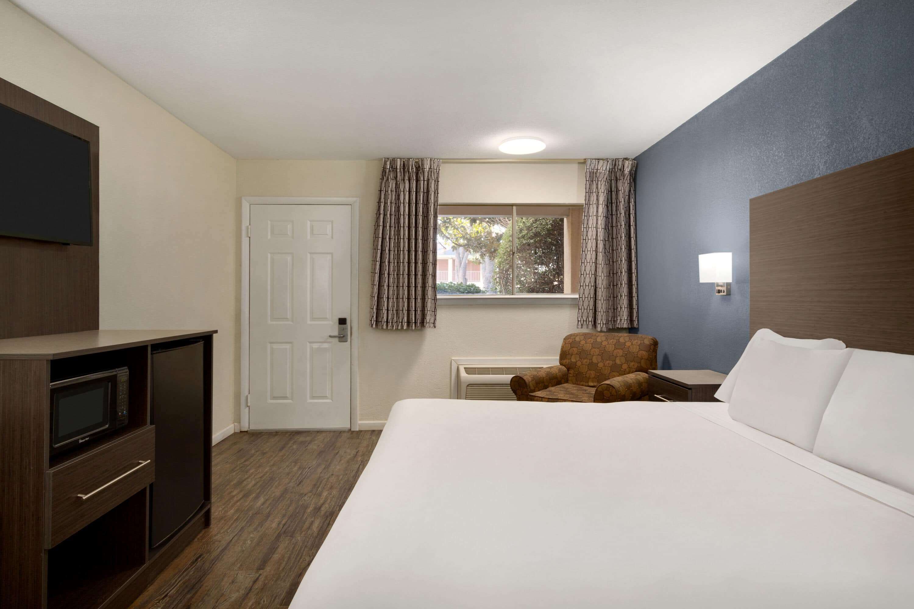 A hotel room with a bed, a TV, a desk, a chair, and a window with curtains.