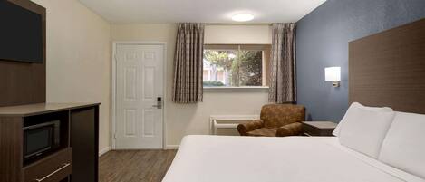Habitación de hotel con cama, televisión, escritorio, silla y ventana con cortinas.
