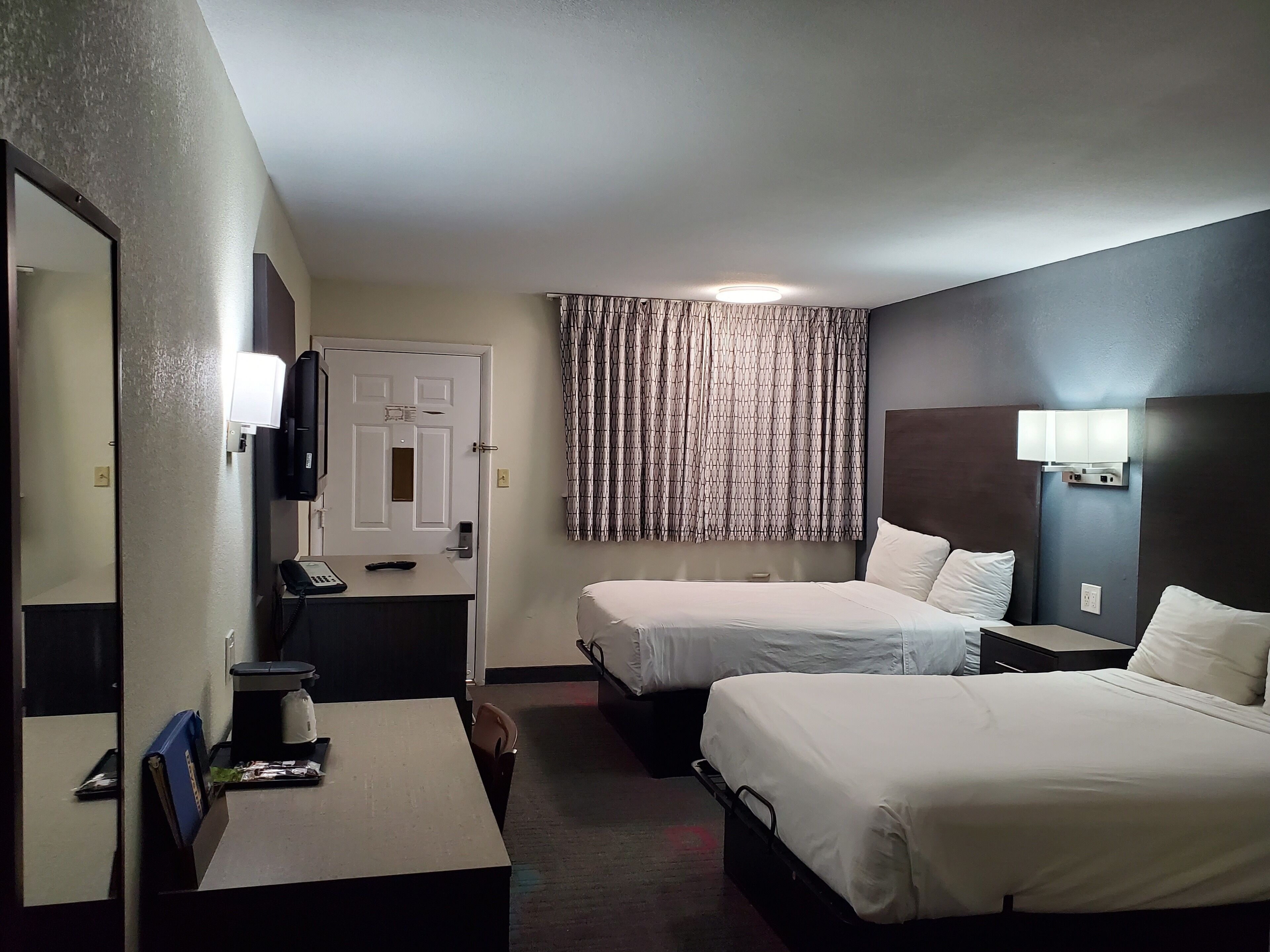 Une chambre d’hôtel avec deux lits, un bureau doté d’un téléphone et d’une machine à café, un miroir et une porte surmontée d’une lumière.