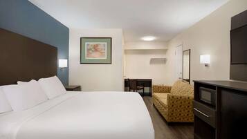 A hotel room with a large bed, a sofa, a desk, a television, and a microwave.