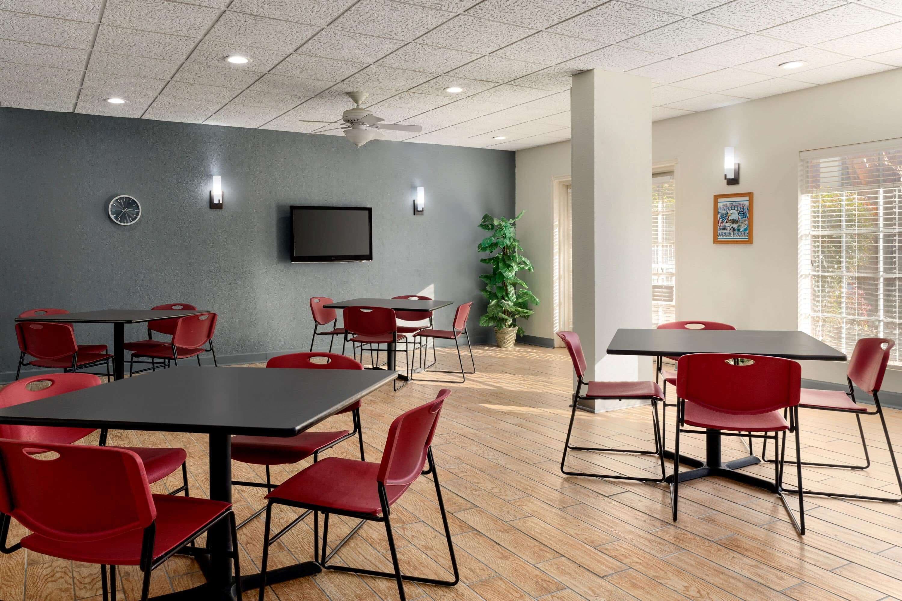 A conference room with tables and chairs, a ceiling fan, a clock, and a television on the wall.