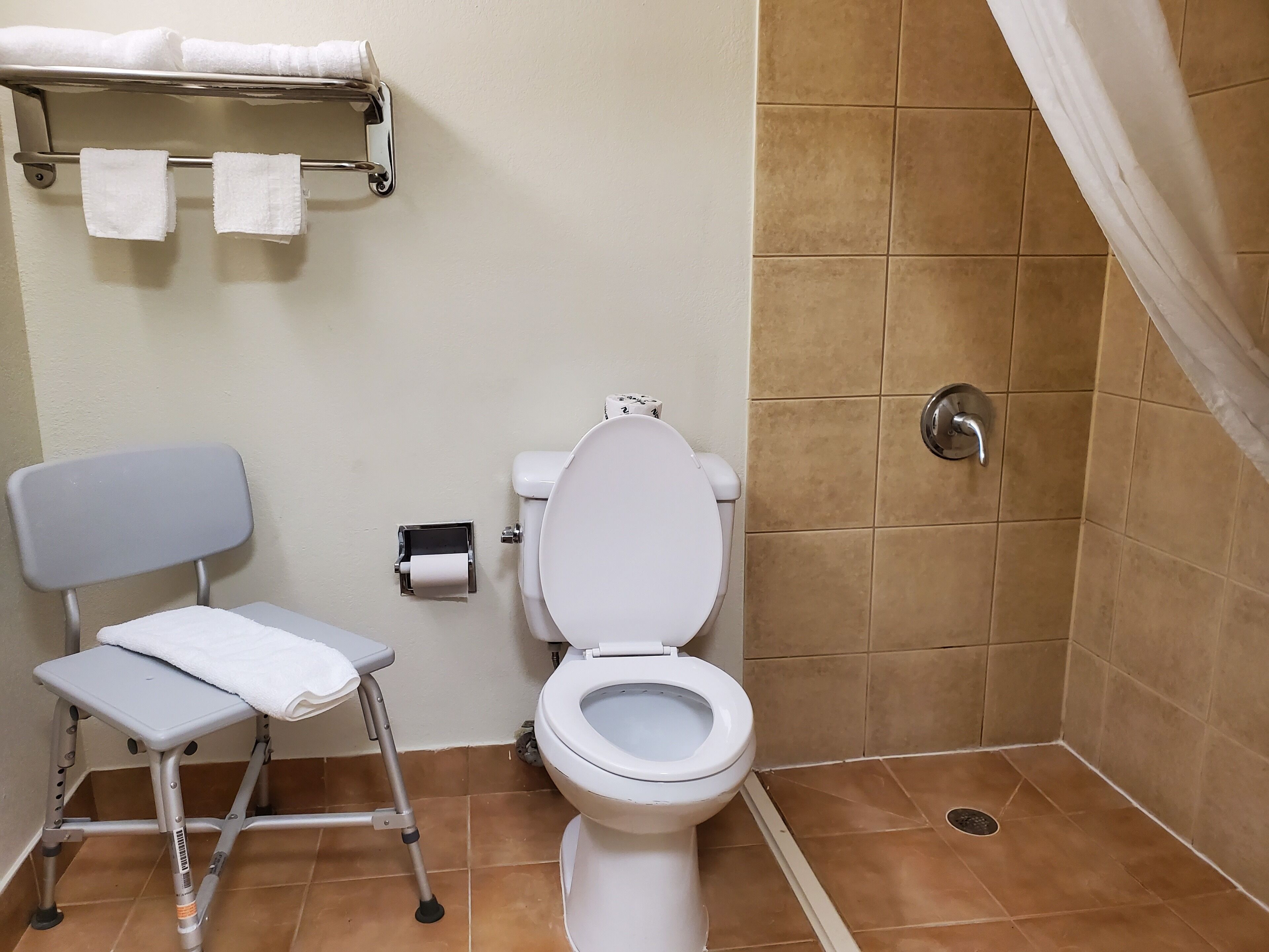 Une salle de bain avec des toilettes, une douche et une petite chaise.