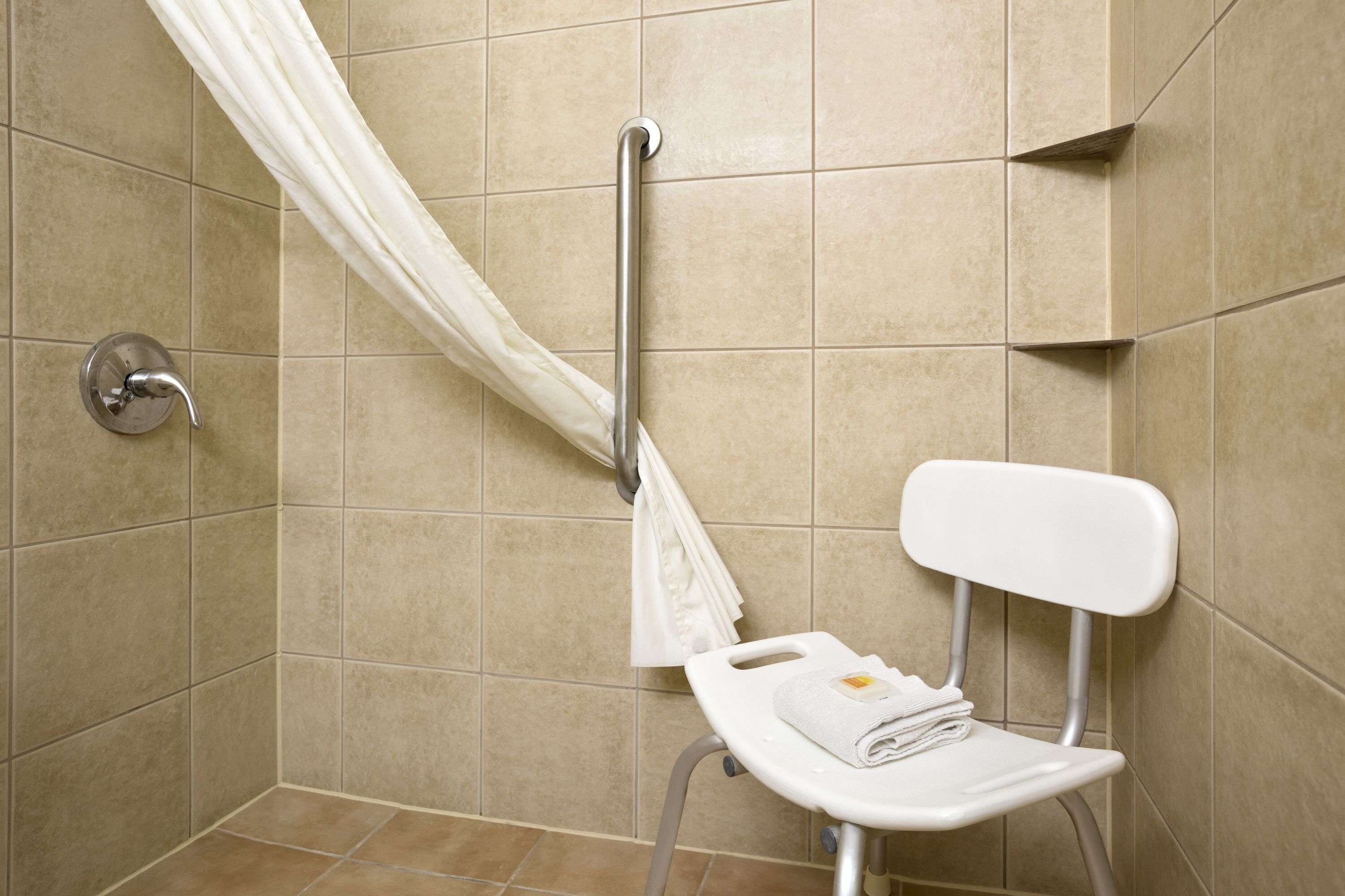 Baño con asiento de ducha, barra de apoyo y barra para toallas.