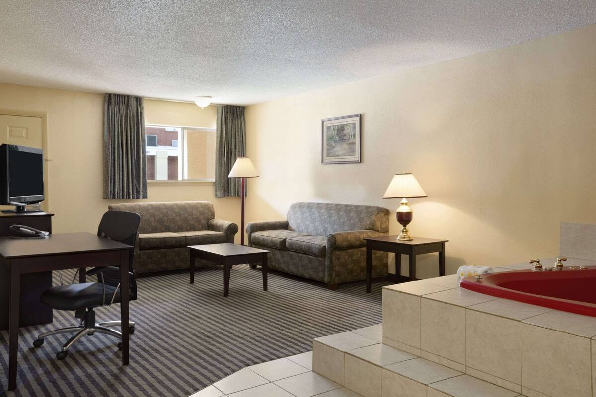 Habitación de hotel con sofá, sillón, escritorio y una bañera roja.