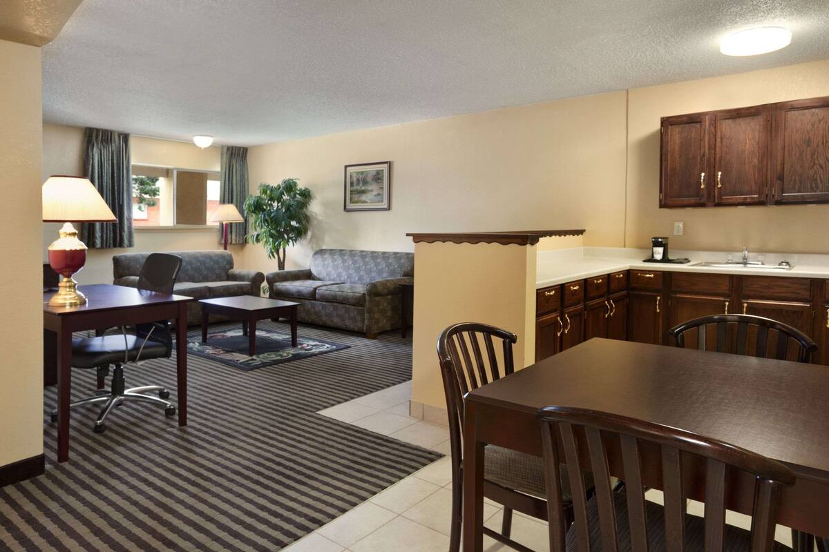 Habitación de hotel pequeña con zona de comedor, sofá, una mesa pequeña y rincón de cocina con armarios de madera.