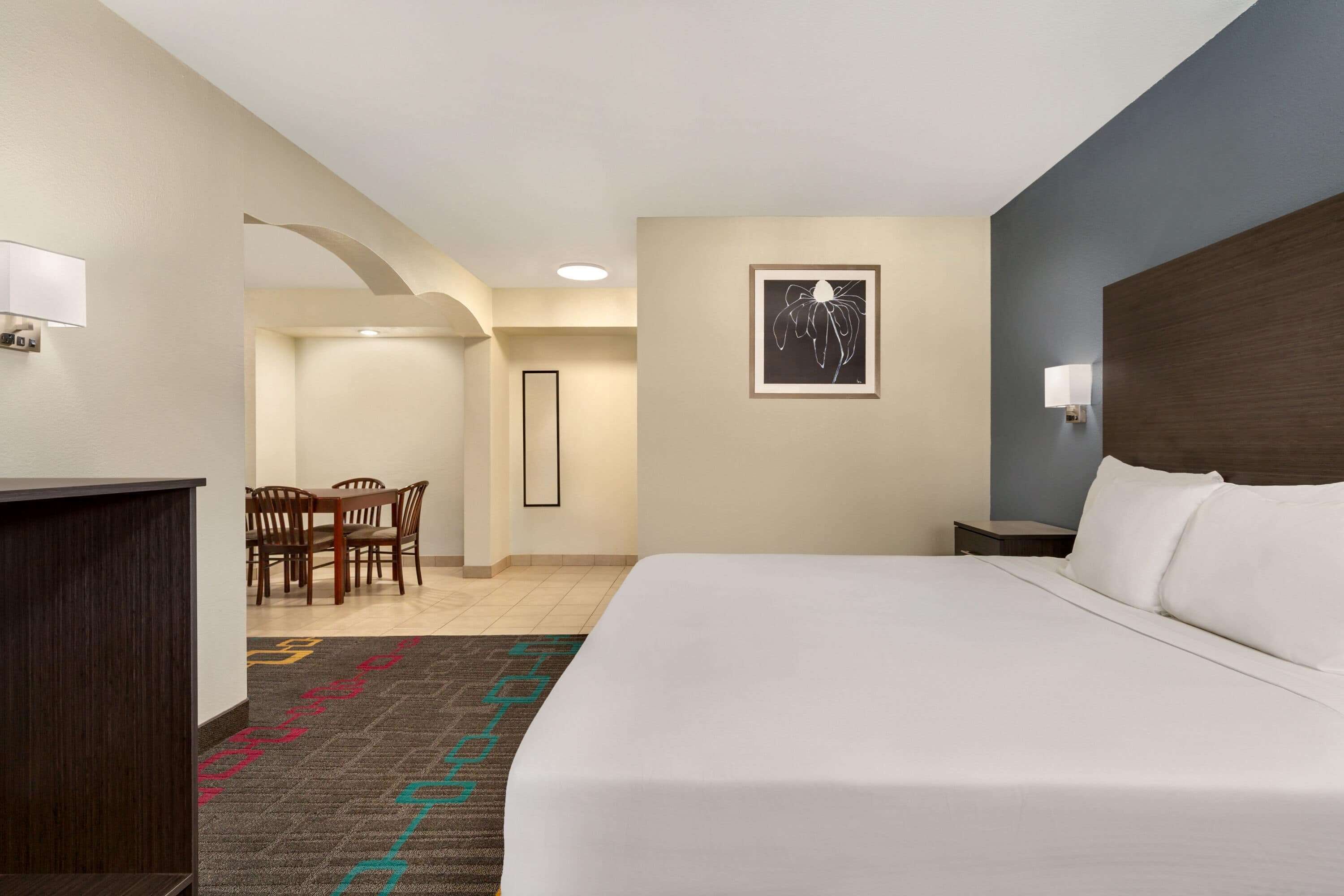 A hotel room with a large bed, a desk, a chair, and a framed picture on the wall.