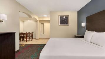 A hotel room with a large bed, a desk, a chair, and a framed picture on the wall.