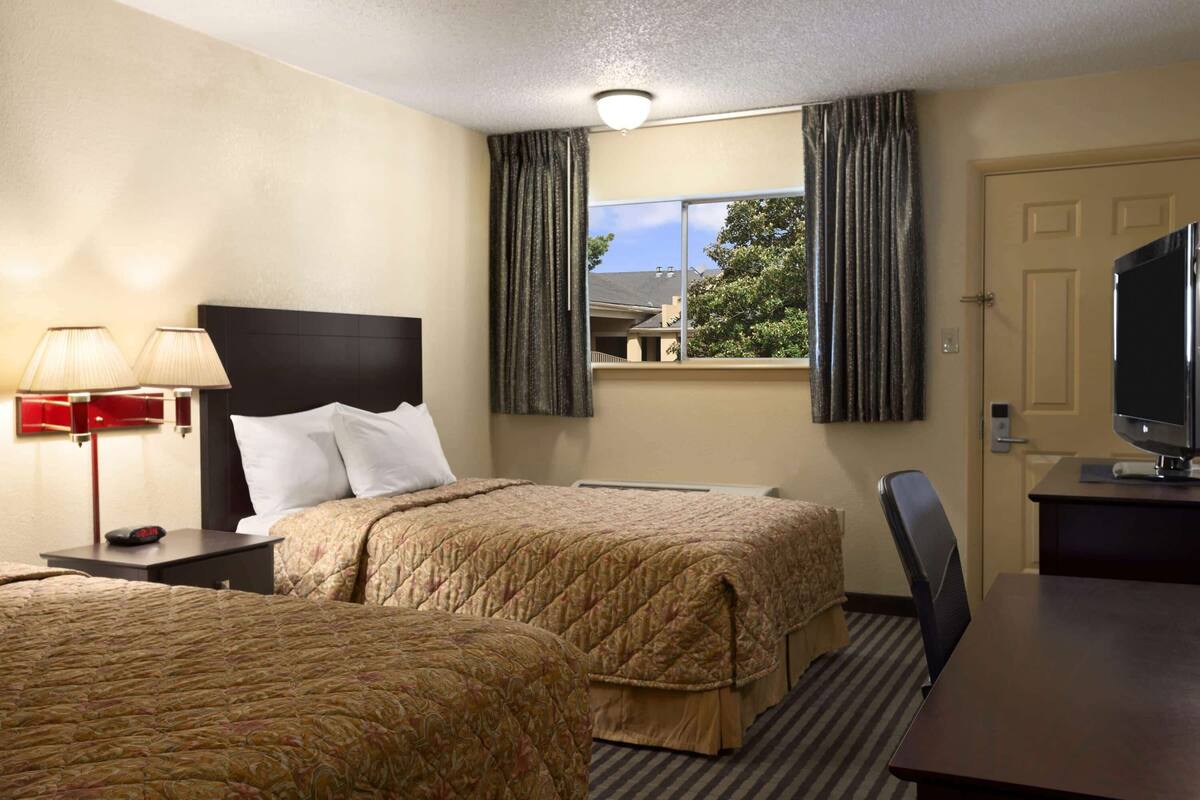Habitación de hotel con dos camas, un escritorio, un televisor, una lámpara y una ventana con cortinas.
