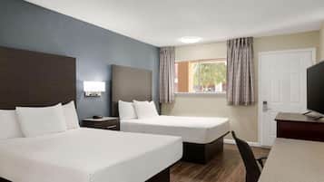 Habitación de hotel con dos camas, un escritorio, una silla, un televisor y una ventana con cortinas.