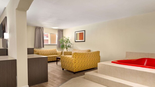 Ein modernes Hotelzimmer mit einer großen, roten Badewanne, zwei gelben Sofas mit Muster und einem kleinen Tisch sowie einer Topfpflanze.
