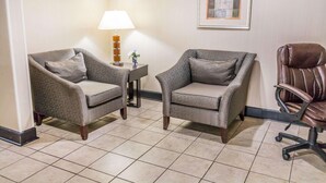 A room with two armchairs, a small side table with a lamp, a framed picture on the wall, and a leather office chair.