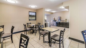 A dining area with tables and chairs, a kitchen in the background, and a sign for Quality Inn.