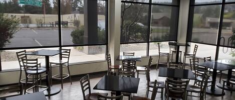 A restaurant interior with multiple tables and chairs, large windows offering views of the street and parking lot.