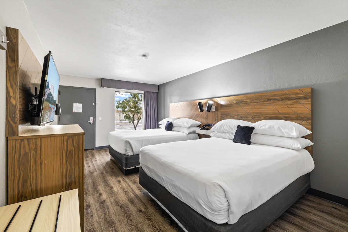 A hotel room with two beds, a wooden headboard, a flat-screen TV, and a desk.