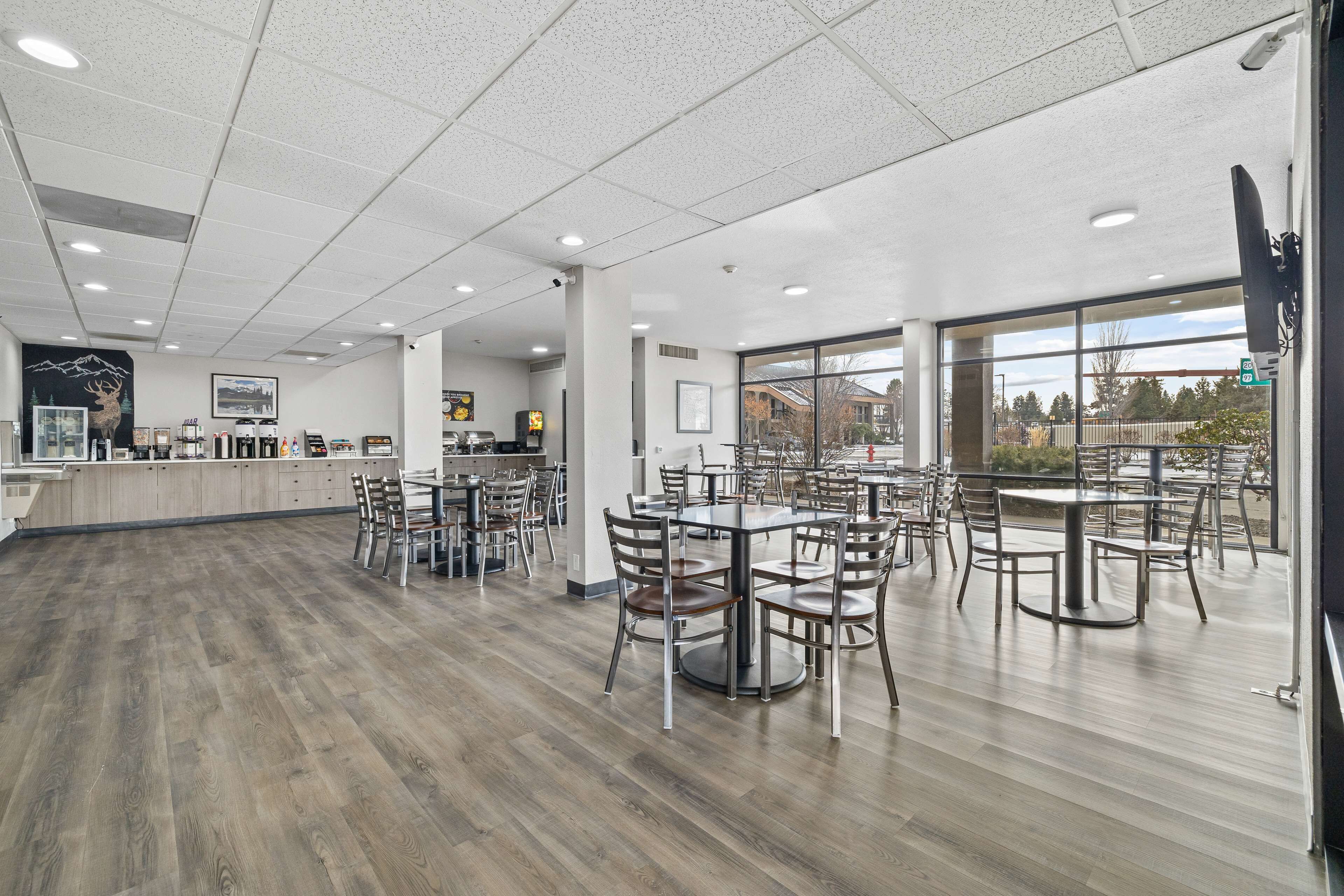 Un espace intérieur vaste et lumineux, avec de nombreuses tables et chaises, un comptoir où sont exposés divers articles, et de grandes fenêtres donnant sur l’extérieur.