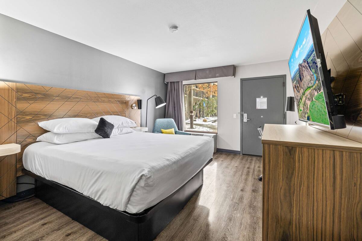 A modern hotel room with a large bed, a desk, a flat-screen TV, and a view of the outdoors.