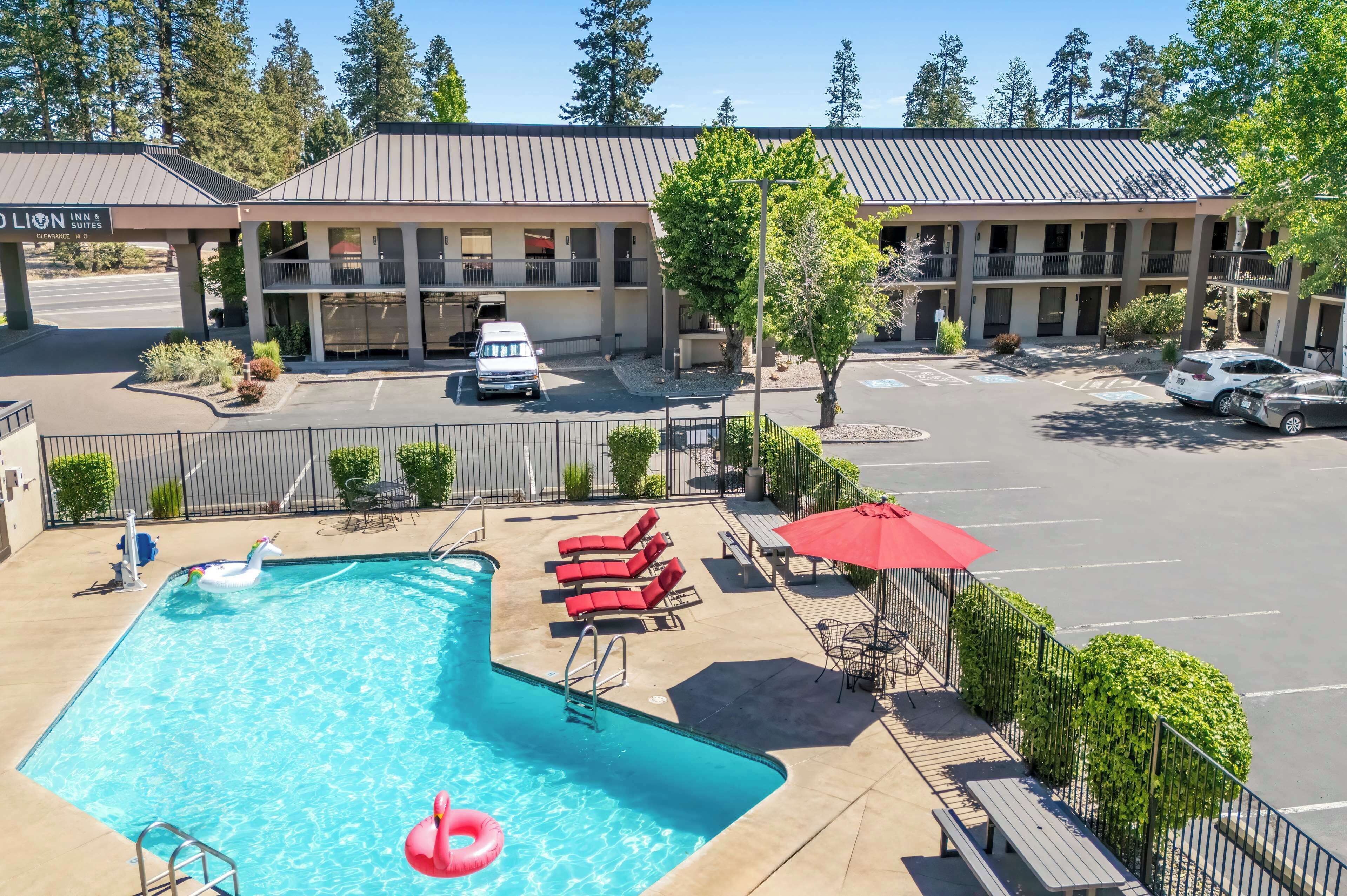 A hotel with a swimming pool, lounge chairs, and a red umbrella.