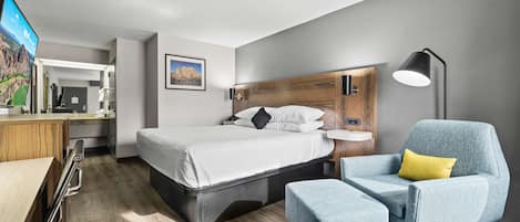 A modern hotel room with a bed, a desk, a chair, and a TV.