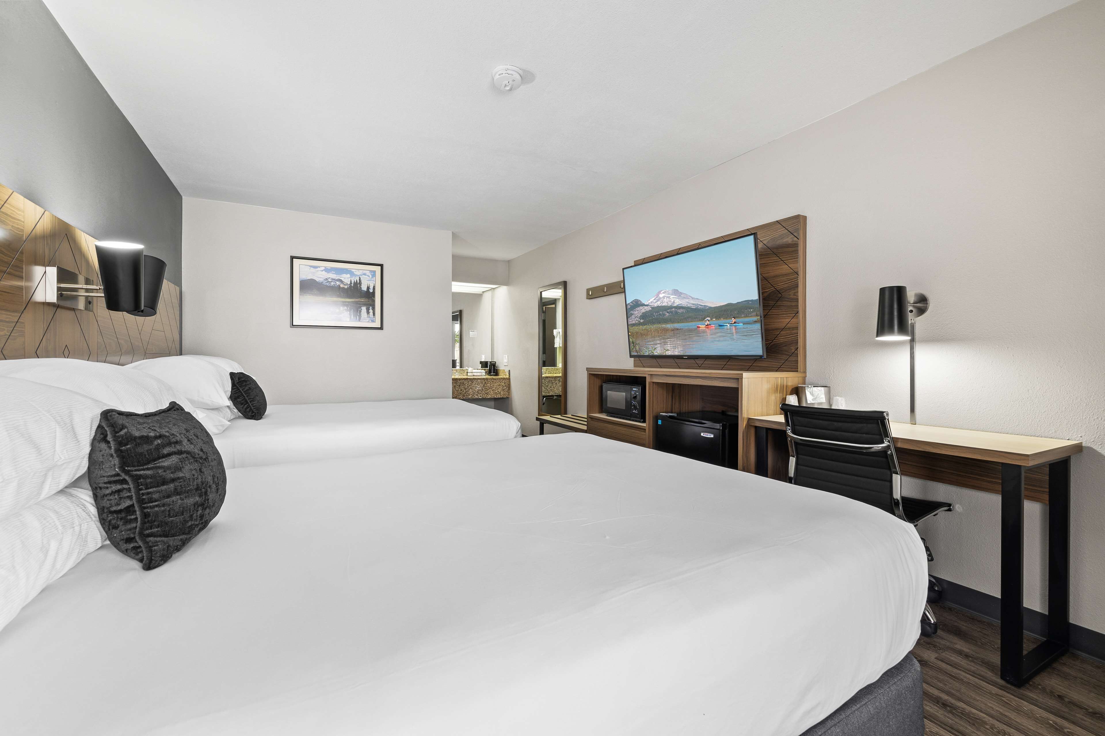Quarto de hotel moderno com duas camas, uma escrivaninha, televisão e vista para uma montanha.